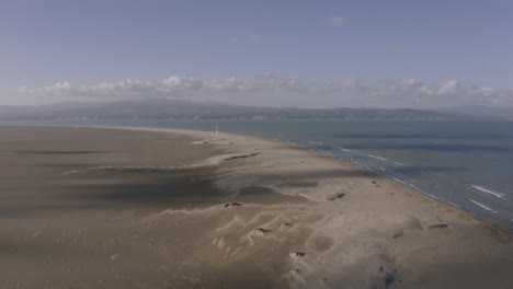High,-wide-aerial-view-of-Delta-del-Ebro-lighthouse-in-distance-with-wide-sand-dunes-of-popular-tourism-spot-in-Spain