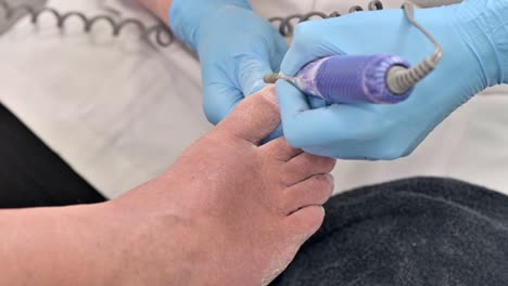 Pedicurist-master-in-blue-gloves-filing-toe-nails-in-the-pedicure-salon-using-e-file
