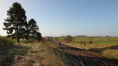 Red-Deutsche-Bahn-train-speeds-through-a-rural-landscape-on-a-sunny-day,-trees-and-fields-in-the-background