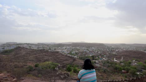 Isoliertes-Mädchen,-Das-Die-Stadtlandschaft-Auf-Einem-Berggipfel-Mit-Dramatischem-Himmel-In-Der-Abenddämmerung-Beobachtet.-Das-Video-Wurde-In-Mehrangarh,-Jodhpur,-Rajasthan,-Indien-Aufgenommen