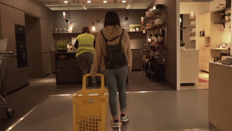 Woman-Pulling-A-Yellow-Rolling-Basket-While-Roaming-Around-In-Ikea-Furniture-Shop