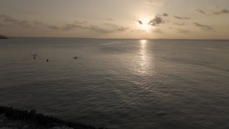 Aerial-view-circling-shimmering-Zanzibar-seascape-to-reveal-people-watching-tropical-sunset-from-Michamvi-beach-coastline