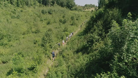 AERIAL-SLOMO:-Runners-running-on-a-trail-through-a-valley-in-a-forest-on-a-sunny,-summer-day