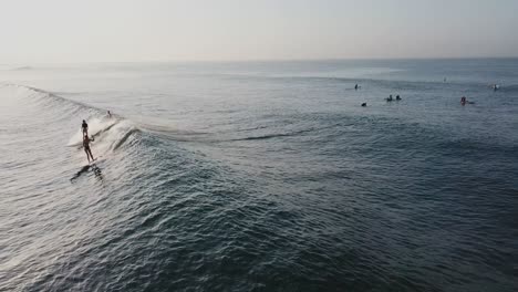 Zwei-Mädchen-Surfen-Mit-Longboards-Auf-Einer-Meereswelle-Während-Des-Sonnenaufgangs-In-Indonesien