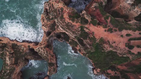 Straight-down-descending-view-of-eroded-rock-formation-of-coastal-cliffs-and-crashing-waves-by-aerial-4k-drone-at-Ponta-da-Piedade-near-Lagos-in-the-algarve-region-of-Portugal