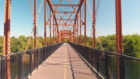A-man-and-woman-walking-and-jogging-on-the-Fair-Oaks-Bridge-over-the-American-River-in-California---Aerial-drone-view-flying-through-the-bridge