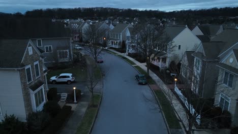 Twilight-scene-of-a-suburban-street,-lined-with-closely-packed-two-story-houses,-cars-parked-along-the-curb,-and-bare-trees