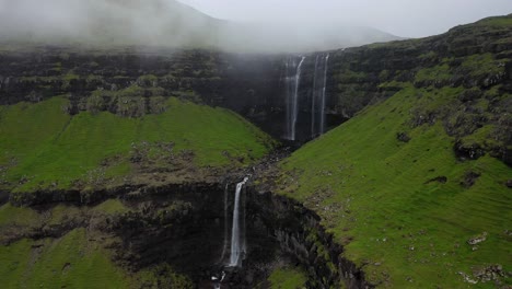 Fossá-Waterfall-sea-cliffs-on-cloudy-Faroe-Islands-coastline,-aerial-pull-away