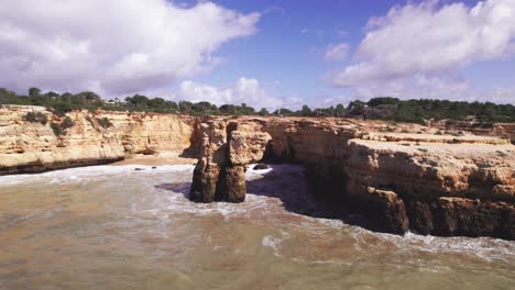 Vista-De-La-Costa-Con-Hermosos-Acantilados-Escarpados-De-Color-Naranja-Con-Un-Arco-Natural-Tallado-Con-Olas-Con-Grupos-De-Excursionistas-Por-Drones-Aéreos-4k-En-La-Playa-De-Albandeira-En-La-Región-Del-Algarve-De-Portugal