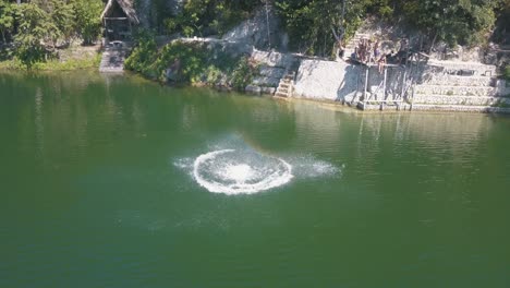 Toma-Aérea-De-Un-Dron-De-Un-Hombre-Saltando-De-Una-Cuerda-Haciendo-Un-Salto-Hacia-Atrás-En-El-Lago-En-Flores-Petén,-Guatemala