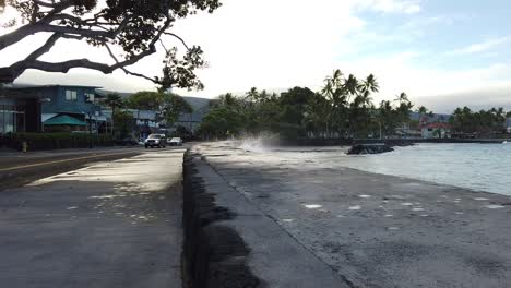 Splashing-wave-against-a-breaker-wall-on-the-beachfront-early-morning-as-cars-drive-by-slowly