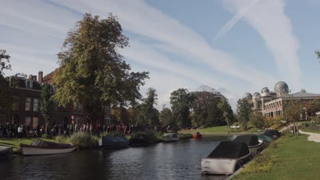 People-lining-the-streets-of-a-canal-in-Leiden,-the-Netherlands,-on-the-annual-3-October-celebration-of-the-Relief-of-Leiden,-with-the-Leiden-Observatory-in-the-background