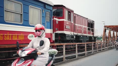 Train-Passing-Through-The-Railway-At-The-Long-Bien-Bridge-With-People-Walking-On-A-Pathway-Lane-Near-Banana-Tree-Island-In-Hanoi-City,-Cau-Long-Bien,-Vietnam