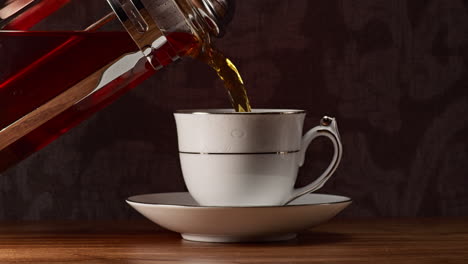 Gießen-Sie-Eine-Heiße-Tasse-Tee-Aus-Einer-Teepresse-Aus-Glas-In-Eine-Weiße-Teetasse-Mit-Untertasse