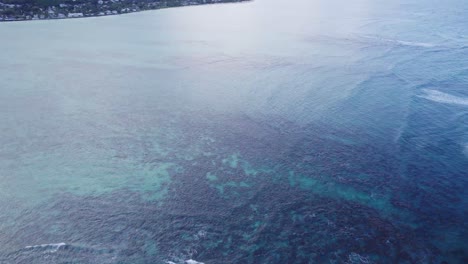 drone-footage-looking-into-the-clear-ocean-water-with-coral-reefs-lining-the-ocean-floor-tilting-up-to-receal-the-coast-of-the-island-of-Oahu-near-Lanikai-Beach-Hawaii