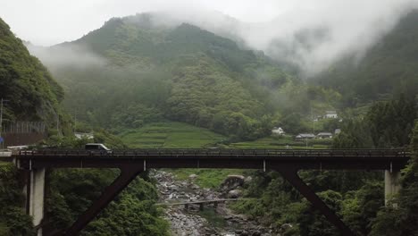 Van-Fährt-über-Eine-Malerische-Brücke-Mit-Nebligen-Bergen-Und-Einem-Fluss-Darunter