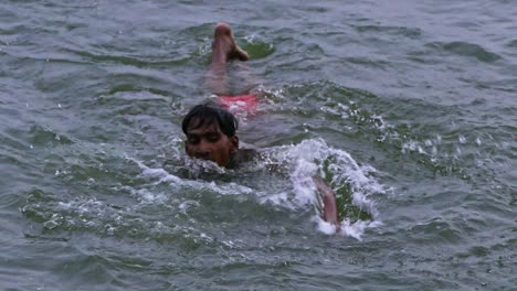 Un-Chico-Aprendiendo-A-Nadar-En-El-Agua-De-Un-Lago-Poco-Profundo-Durante-El-Día-En-Varanasi,-Uttar-Pradesh,-India