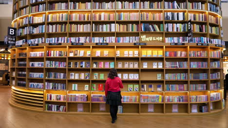 Traveling-Woman-Walks-Toward-Floor-to-ceiling-Bookshelf-At-Starfield-Library-Coex-Mall-In-Seoul,-South-Korea