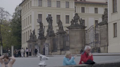 Visitors-walk-by-ornate-statues-outside-Prague's-historical-building,-cloudy-day