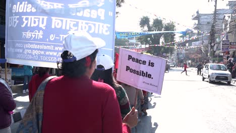 Zeitlupenvideo-Vom-Rücken-Einer-Alten-Frau,-Die-Mit-Einem-Schild-„Friede-Ist-Möglich“-Bei-Einer-Kundgebung-Am-Eröffnungstag-Des-21.-Straßenfestivals-In-Pokhara-Läuft