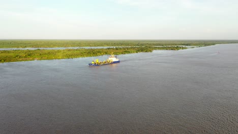 Aerial-Forward-Approach-of-Commercial-Ship-Sailing-Out-Of-Barranquilla-Port-On-The-Magdalena-River-During-Golden-Hour-Sunset