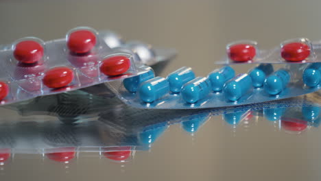 Schwenkansicht-Von-Blauen,-Roten-Und-Weißen-Pillen-Und-Verschreibungspflichtigen-Medikamenten-Auf-Einem-Reflektierenden-Tisch