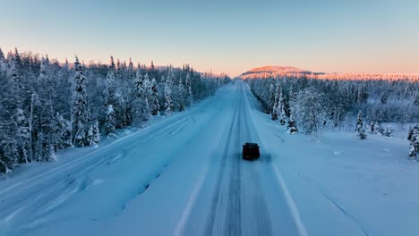 Aerial-view-following-a-SUV-driving-on-a-snowy-road,-in-arctic-wilderness-of-Lapland