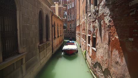Boat-navigating-through-narrow-canal-with-big-residential-buildings-in-Venice