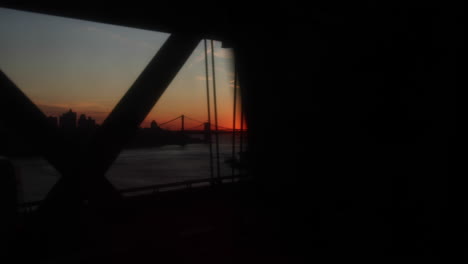 Stunning-slow-motion-shot-of-train-ride-during-sunset-across-the-Williamsburg-bridge,-connecting-Brooklyn-and-Manhattan-in-New-York-City