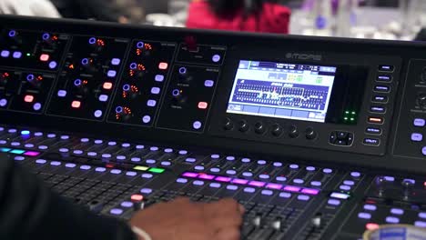 Close-up-of-a-hand-adjusting-controls-on-a-digital-audio-mixer,-colorful-buttons-illuminated