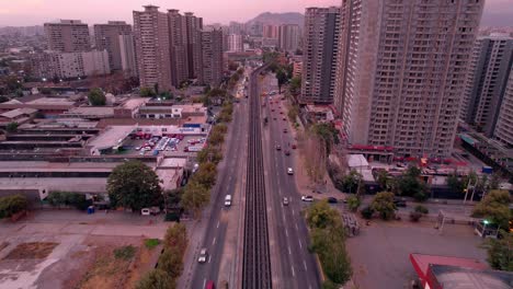 Drone-flyover-Subway-tracks-between-road-traffic-at-sunset,-Santiago-downtown,-Chile