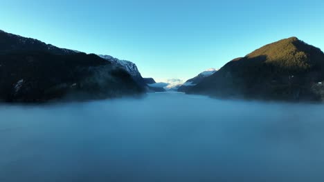 Flying-into-morning-fog-hovering-over-Norway-sea,-Veafjord-in-background