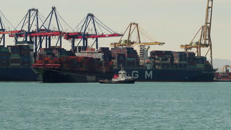 Tow-boats-carrying-cargo-ship-full-of-containers-for-departure-from-port-of-Valencia,-Spain