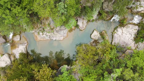 Beautiful-aerial-shot-of-a-river-stream-surrounded-by-big-rocks-and-trees,-drone-footage