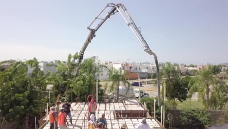 Aerial-view-of-construction-workers-working-on-the-roof-pouring-cement-from-a-truck-crane-to-build-roof-or-floor-structure-wearing-orange-vests