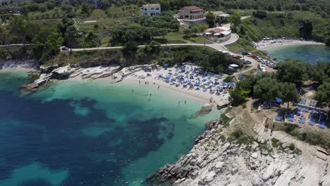 Aerial-view-dolly-left-showing-people-swimming-and-sunbathing-beautiful-turquoise-sea,-bright-sunny-day-Kassiopi-Corfu-Greece