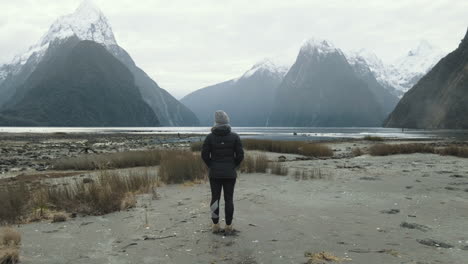 Chica-Parada-Sola-Frente-A-Imponentes-Montañas-Cubiertas-De-Nieve-Y-Fiordos-En-Milford-Sound-De-Nueva-Zelanda