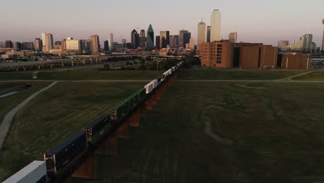 Aerial-of-Freight-Train-Headed-into-Downtown-Dallas-Texas-at-Sunset-City-Skyline-in-the-Background