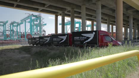 Fleet-of-HSM-Global-delivery-vehicles-parked-under-bridge-near-port,-riser-shot