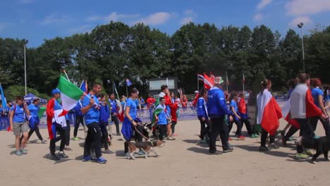 Participants-From-Different-Countries-Waving-National-Flags-With-Their-Pet-Dogs-At-European-Open-Juniors-Championship---Agility-Competition-In-Netherlands---panning-shot
