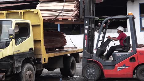 Worker-operating-forklift-beside-yellow-truck