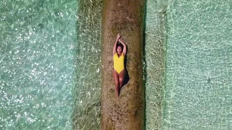 Aerial,-top-down,-drone-shot,-of-a-woman,-in-a-yellow-swimsuit,-laying-on-sand,-surrounded-by-the-turquoise-sea,-on-a-sunny-day,-on-the-Conrad-Rangali-island,-in-Maldives