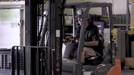 Man-turning-forklift-truck-and-laughing-within-warehouse-4K