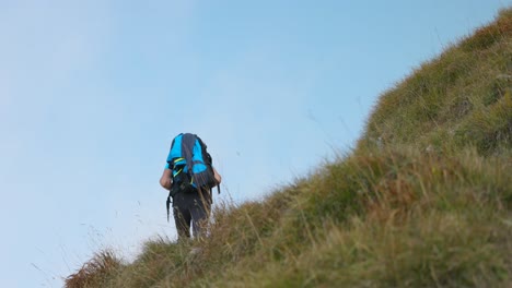 Rear-view-hiker-with-backpack-walks-on-hiking-trail-through-grassy-slopes
