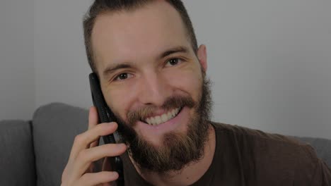 Hübscher-Europäischer-Junger-Mann-Mit-Bart-Ruft-An-Und-Lächelt,-Nachdem-Er-Gute-Nachrichten-Von-Seinem-Smartphone-Gehört-Hat