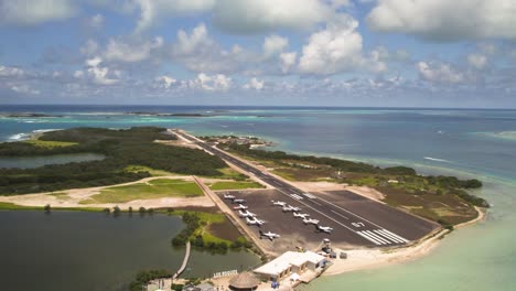 Gran-Roque-Los-Roques-Landebahn-Mit-Geparkten-Flugzeugen-Und-Türkisfarbenem-Wasser,-Sonniger-Tag,-Drohnenaufnahme,-Luftaufnahme