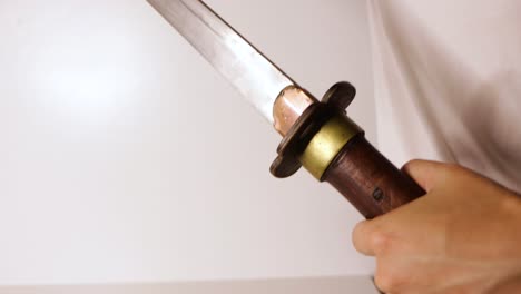 Pulling-antique-sword-from-sheath-in-white-room-close-up