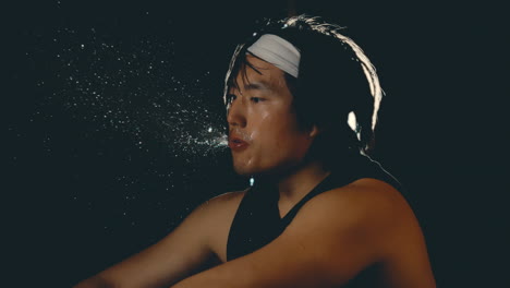 Asian-male-athlete-spitting-water-in-slow-motion-after-hard-workout-in-dark-gym,-backlit-close-up-4k-800fps
