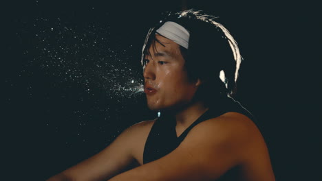 Asiatischer-Männlicher-Athlet-Spuckt-Wasser-In-Zeitlupe-Nach-Hartem-Training-Im-Dunklen-Fitnessstudio,-Nahaufnahme-Mit-Hintergrundbeleuchtung,-4K,-800 fps