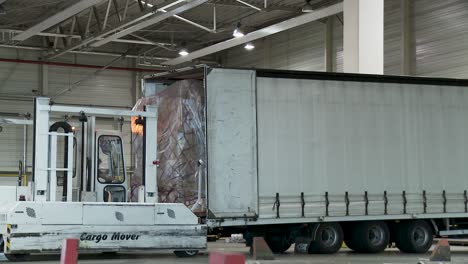 Forklift-loading-cargo-onto-a-truck-in-an-industrial-warehouse,-daytime,-active-logistics-scene